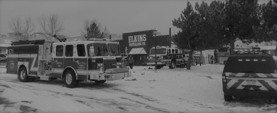 A black and white image shows firetrucks in front of Elkins Building.